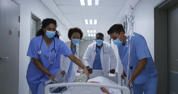 Diverse female and male doctors wearing face mask transporting patient