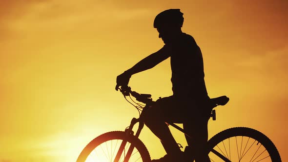 Silhouette of professional bicyclist taking a bottle and drinking water at golden sunset.