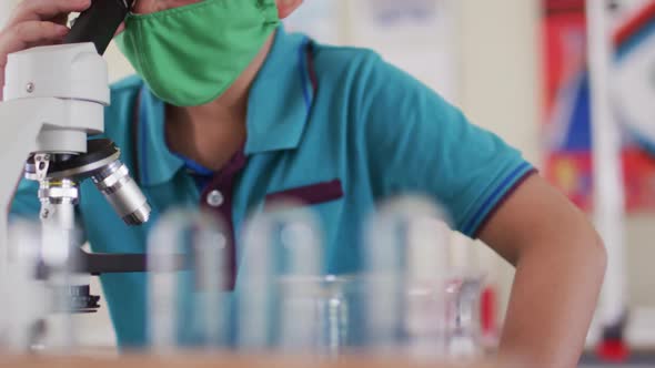 Boy wearing face mask and protective glasses using microscope in laboratory