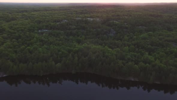 Aerial drone shot flying up and tilting downwards over the forest next to Charletston Lake in Ontari