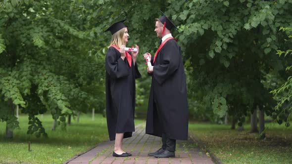 Smiling Male and Female Graduates Talking in Park After Graduation Ceremony