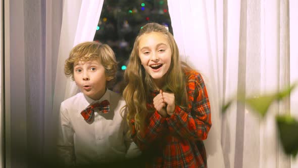 Portrait of Excited Brother and Sister Standing Behind Glass Looking Out Window Pointing Looking