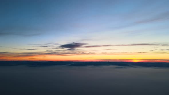 Aerial View of Colorful Sunset Over White Dense Foggy Clouds Cover with Distant Dark Silhouettes of