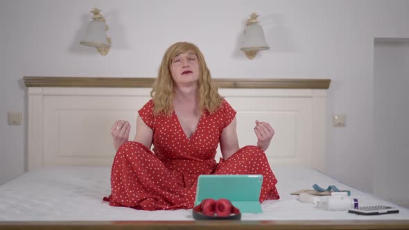 Wide Shot Front View Relaxed Trans Woman Meditating with Eyes Closed Sitting on Bed at Home