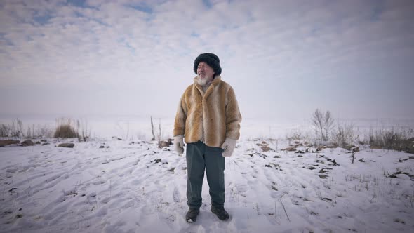 Wide Shot Front View Old Bearded Indigenous Man Standing at Arctic Ocean Shore with Cloudy Sky at