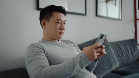 Smiling Asian man texting by phone