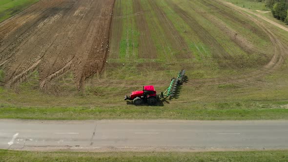 Farmer on a Tractor Turns Around Near the Road and Begins Plowing Farmland in Spring in Sunny