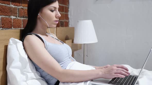 Relaxing Woman Enjoying Listening Music on Laptop in Bed