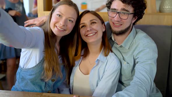 Three Friends Sit in a Cafe Have Fun Communicating and Make Selfie