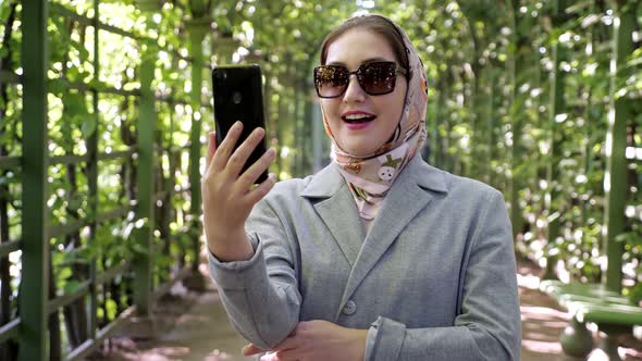 Woman in Headscarf and Sunglasses Talking on the Phone Via Video Link in the Garden Arch