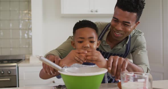 African american father teaching his son how to crack eggs while baking in the kitchen at home