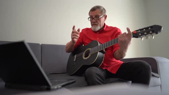 Portrait of a Grayhaired Mature Man in a Red Shirt and Glasses Playing the Guitar While Sitting on