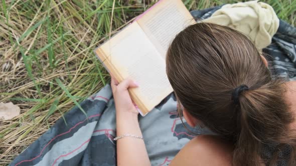 Young Woman Reads a Book Lying in the Grass on Nature at Summer Day.