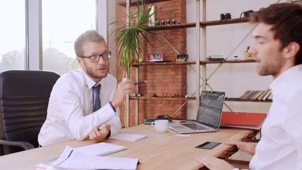 Confident Caucasian Male Boss in Glasses and White Shirt Explaining Something to Office Worker with