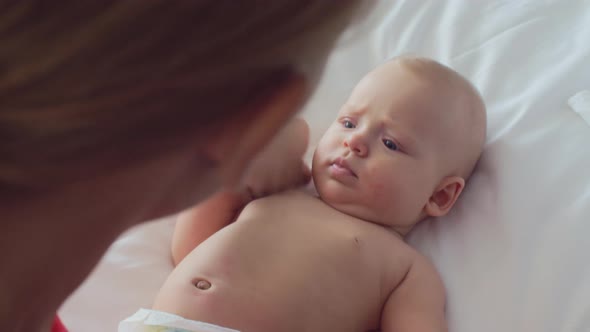 A mother playing with a 6 months old girl, who is lying on a bed