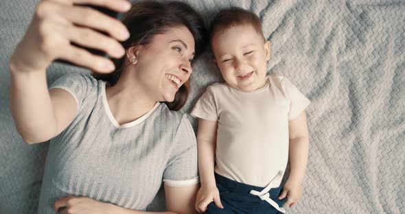 Laughing Woman and Baby Boy Making a Selfie or Video Call in a Bed