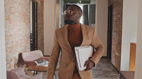 African American Businessman with Documents Walking along Office