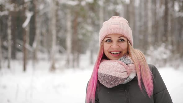Woman in a Jacket and Hat in Slow Motion Looks at the Snow and Catches Snowflakes Smiling