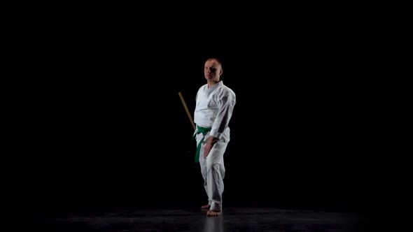 Kendo Fighter on White Kimono Practicing Martial Art with the Bamboo Bokken on Black Background