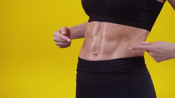 Woman points fingers at a muscular belly in the studio, close-up. Sporty woman shows off muscular