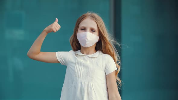 Little Girl Wears Protective Medical Mask From Virus, Shows Thumb Up To Camera, Sign of Consent