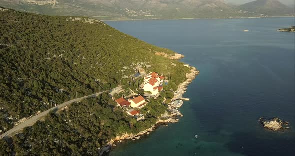 Aerial video tracking along the coast line of a small island with mainland, mountainous hills, in th