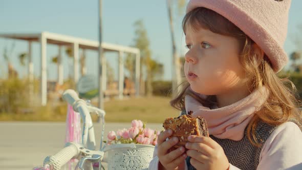 Сute Fashionable Little Girl Eats Cake In The Park