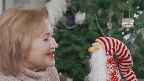 Cheerful Senior Woman Laughing to the Camera Holding Funny Toy Santa Claus