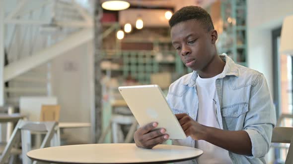 Cheerful African Man Working on Tablet in Cafe