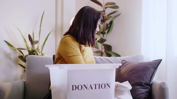 Woman selecting clothes for donation and putting in box.