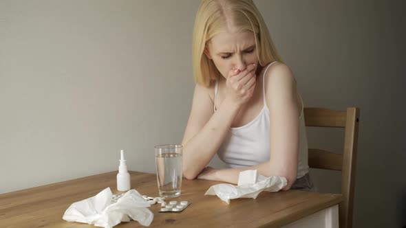 Medium Shot of Blond Woman with Sore Throat Sitting at Kitchen Table and Coughing