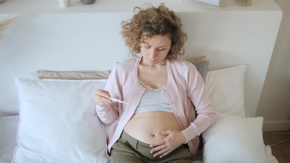 Sad Sick Pregnant Woman Taking Temperature With Thermometer On Bed.