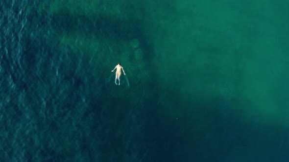 Top View of a Woman in a Yellow Swimsuit Swimming in the Sea with Clear Water