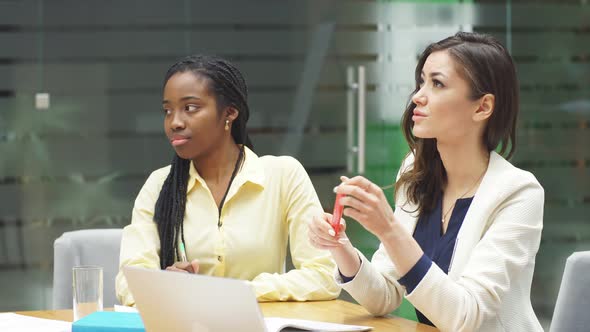 Young African-American Woman Is Sitting at a Desk in the Office and Discussing Working Moments with