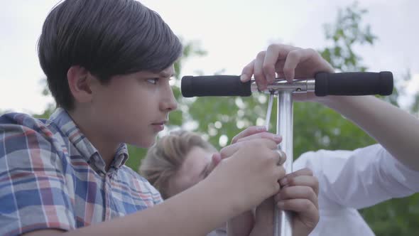 Young Father Teaching His Son To Fix Scooter Close-up. Side View of Cute Boy with Screw Driver