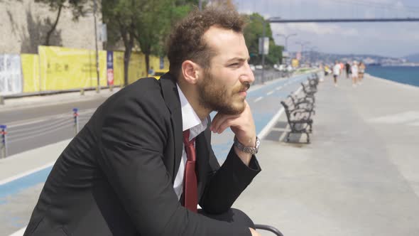 Bored businessman sitting on bench by the sea in the city.