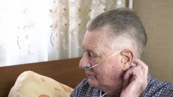 Elderly Person Puts a Nasal Catheter with Oxygen on His Head at Home