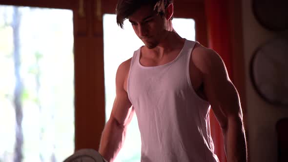 Tight shot of teen body builder in home environment curling large mass of weights.