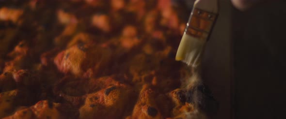 Chef spreading olive oil over freshly baked pizza dough with tomato sauce. Close up, slow motion.