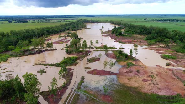 Drone flight over cloudy red clay waters and landscape towards flat green plains, Dominican Republic