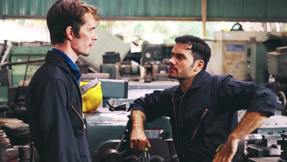 Tired Factory Workers Taking a Break and Talking to Coworker in the Factory