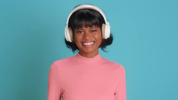 Young Mixed Race Woman Smiles Broadly Listens Music in Headphones Over Blue Wall