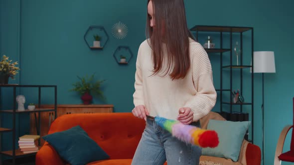 Joyful Young Woman Dusting Furniture Caring for Hygiene Using Colorful Duster in Living Room at Home