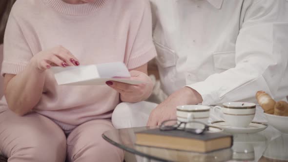 Unrecognizable Caucasian Mature Woman Opening Letter at Home, Mature Man Hugging His Upset Wife, Old