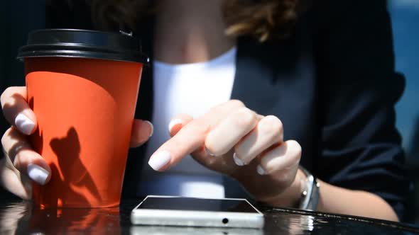 Closeup of Beautiful Young Business Female Hands Scrolling Smart Phone in Cafe with Cup of Coffee