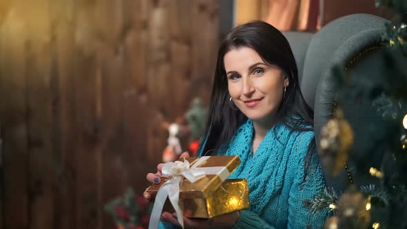 Smiling Brunette Woman Opening Gift Box Over Lights of Christmas Tree