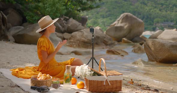 Pretty Woman in Hat and Yellow Dress Having Video Conference with Her Clients on Sunny Desert Beach