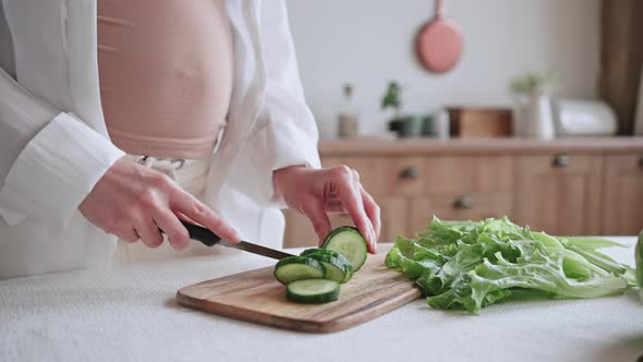 Pregnant Woman Cuts Fresh Cucumber Near Lettuce at Table