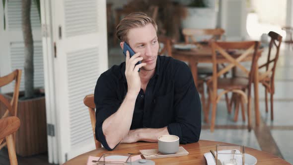 Portrait of Handsome Man Drinking Coffee in Modern Cafe and Talking on Phone