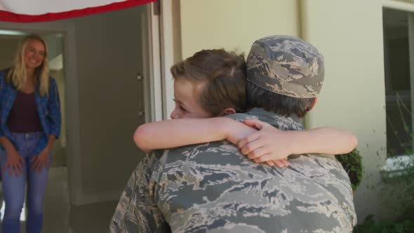 Caucasian male soldier embracing his smiling son over wife and american flag